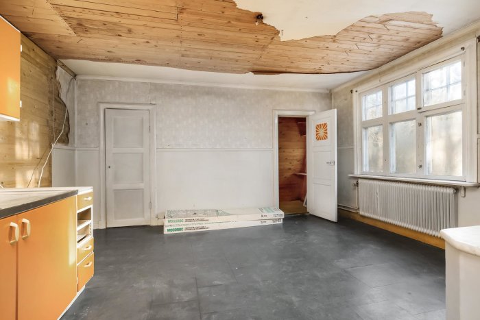 Renoveringsbehovigt kök med osäkrat tak, vita väggar och orange köksinredning.