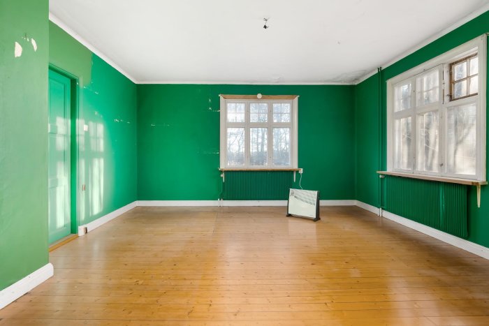 Gammalt tomt rum med gröna väggar och trägolv, belysning från fönster.