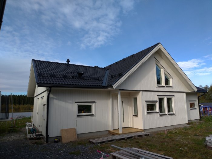 Ett vitt hus med svart tak, avluftningsrör på nocken, omgivet av en byggarbetsplats.