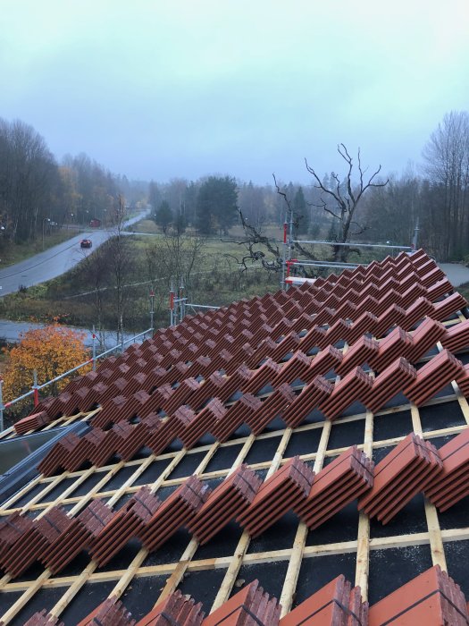 Nyligen konstruerat hustak med röda takpannor och träspånskivor intill en väg.