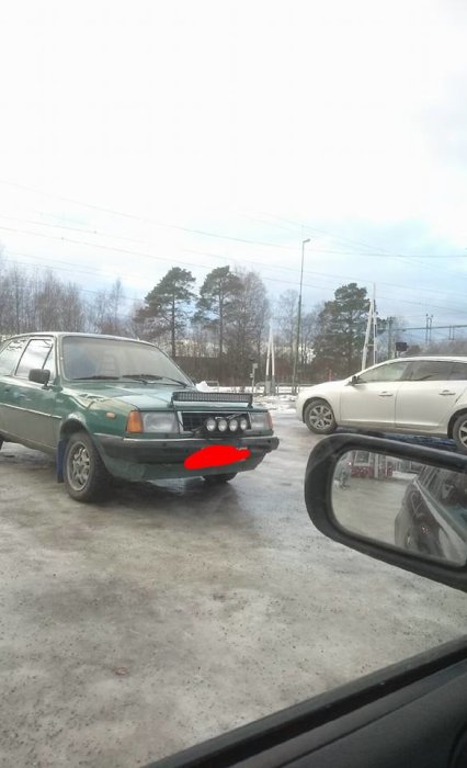 Grönt fordon med extraljus ovanpå motorhuven parkerat på en parkeringsplats.