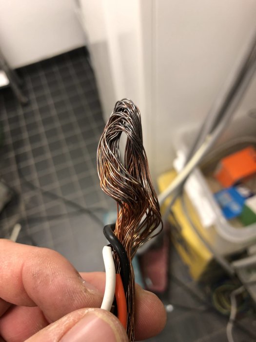 Närbild på en hand som håller sammanflätade kopparkablar med missfärgningar och isolerade ledningar.