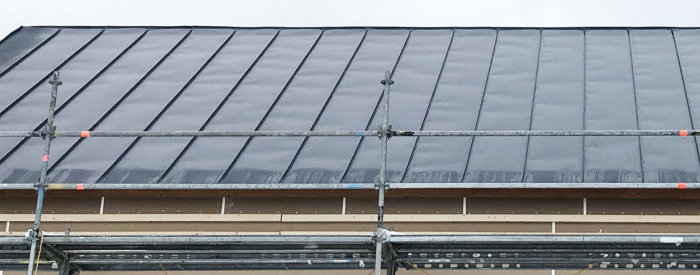 Buckligt bandtak på ett hus i byggfas, synliga vågor och ojämnheter på takplåtarna.