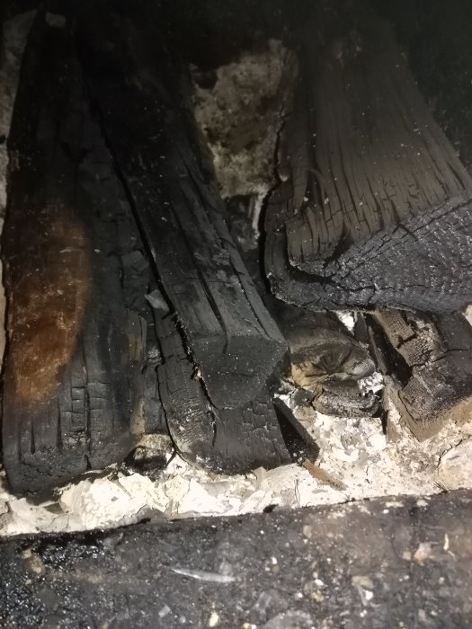 Insida av en panna med brända vedträn och aska, redo för ny tändning.