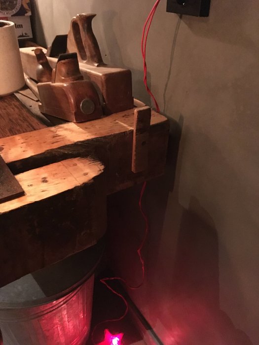 Hyvelbänk med trähyvlar och en okänd vikbar träbit till höger, röd ledning hänger nära.