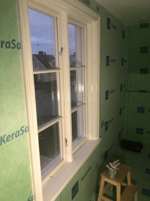 Nyinstallerad fönsterbräda och foder runt fönster i ett badrum under renovering, med verktyg och målarburk.