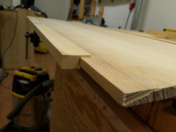 Närbild av träsnitt med halvuppställt haunched tenon på ett arbetsbänk i en verkstad, med verktyg i bakgrunden.