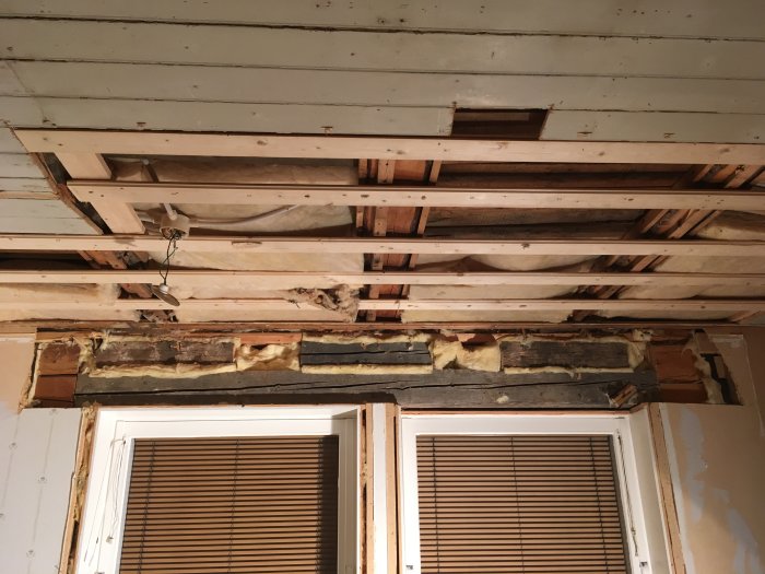 Vanhan talon sisäkaton ja seinän rakenne, paljastettu puupalkit ja eristys. Näkyvissä ikkunan yläpuolella, osia katon materiaalista puuttuu.