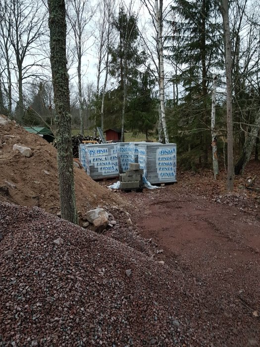 Stomme till garage med pulpettak under konstruktion, omgiven av skog och grusmark.