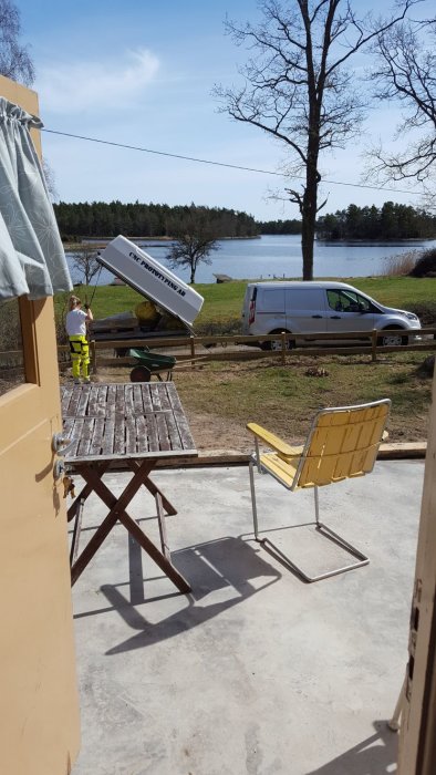 Vy från en renoverad glasveranda mot sjö med person och skåpbil i arbete utanför.