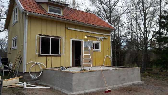 Renoveringsarbete på en glasveranda vid ett gult hus med verktyg och byggmaterial synligt.