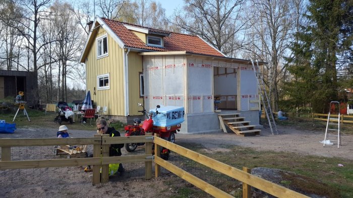 Renovering av glasveranda på gult hus med byggmaterial och stege, famn på landet.