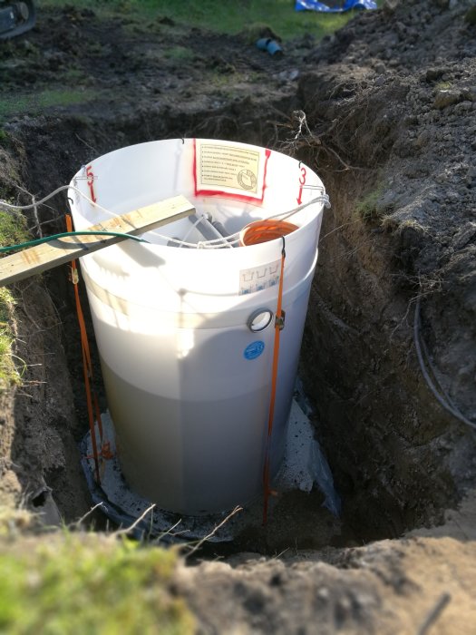 Aquatec avloppssystem som installeras i marken, omgiven av grävd jord och säkrad med rep.