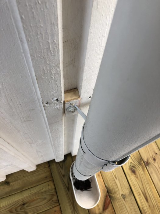Någon står vid hörnet av ett nyproducerat hus och inspekterar en dörrstolpe med synliga skruvhål och slitage.