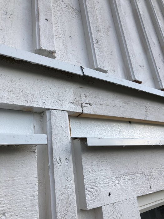 Närbild av skadad vit träpanel på nytt hus med synliga sprickor och flagande färg.
