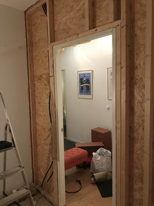 Rivningsarbete av en inomhusvägg med synliga reglar och elledningar, omgiven av byggmaterial.