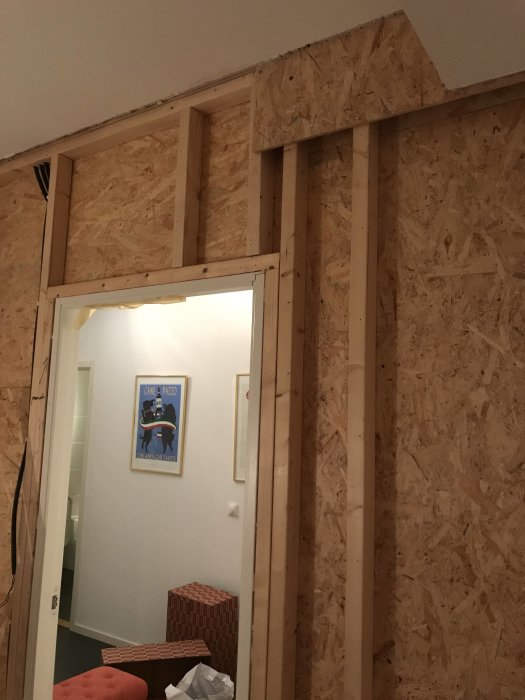 Delvis rivet väggparti med synliga stående och horisontella träreglar och OSB-paneler.