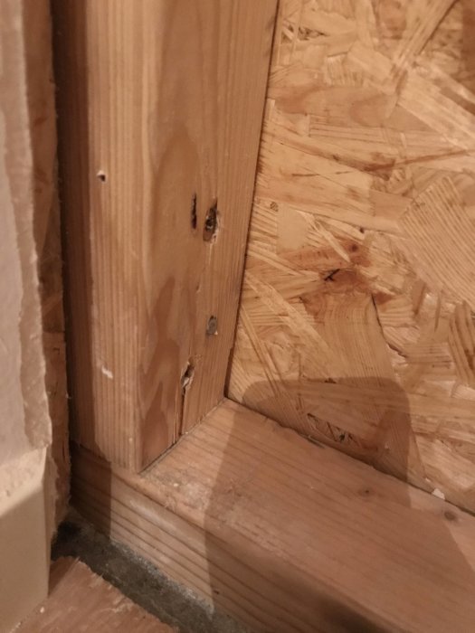 En träregel som sticker ut cirka 1 cm från en OSB-skiva i hörnet av ett rum under renovering.