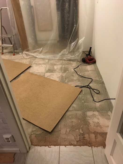 Ett rum med borttagna klinkerplattor och en röd borrhammare på golvet, redo för renovering.