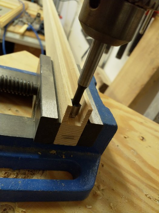 Träsnittarbete med borr som formar ett tapphål i en fastklämd träbit på en arbetsbänk.