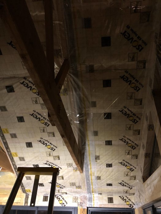 Tak med plastfolie delvis installerad för isolering, träsparrar och en stege i förgrunden.
