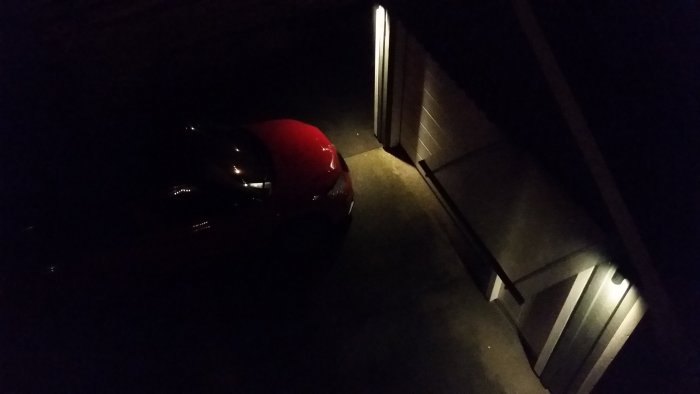 Mörk bild på en parkerad bil vid en garageuppfart med dimlysta omgivningar före användning av strålkastare.