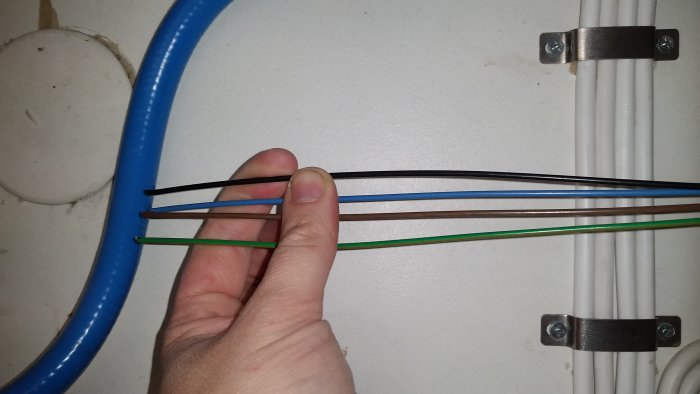 Hand håller upp elektriska kablar med 3G1,5 och 4G1,5 dimensioner med en helgrön jordledare framför vit vägg.