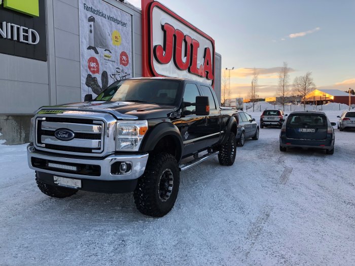 Ford F-250 Super Duty parkerad på snöig parkering, stora 37 tums däck och 6 tums höjning, i skymningen.