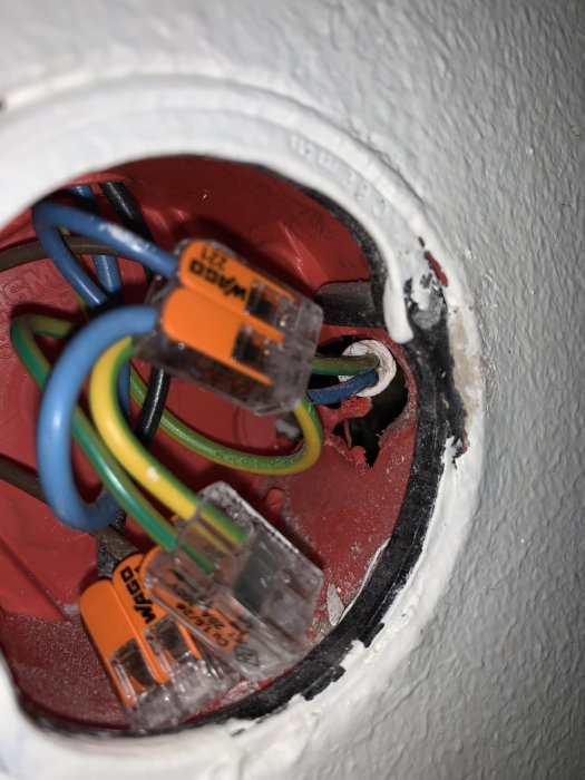 Elkablar i kopplingsdosan bakom en avlägsnad väggkontakt med WAGO-klämmor för anslutning.