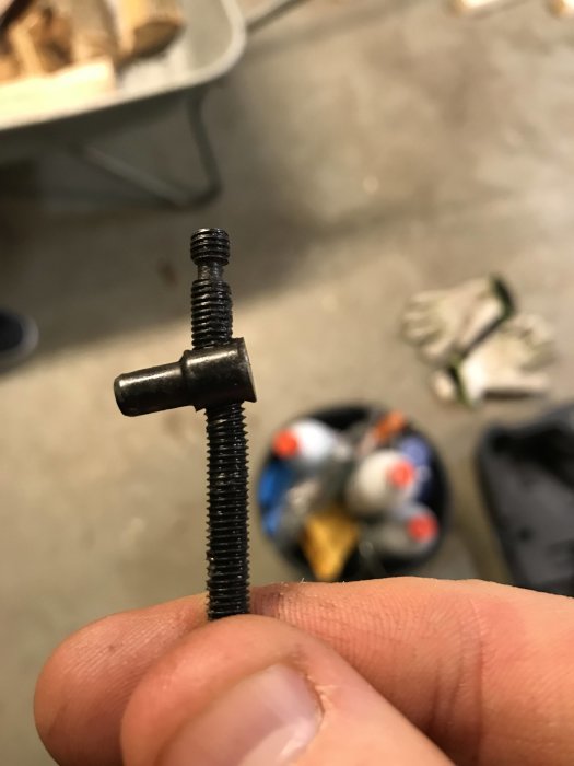 Närbild på en böjd kedjespänningsskruv hållen mellan fingrar.