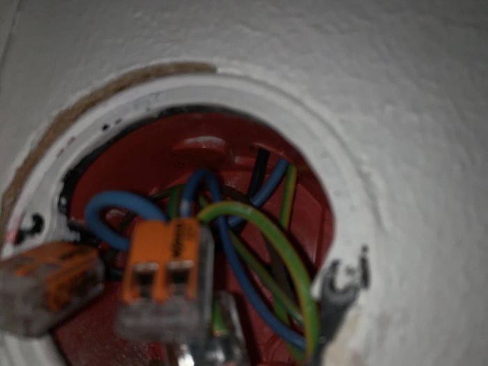 Öppet eluttag med flera elektriska kablar och anslutningsklämmor inuti en vägg.