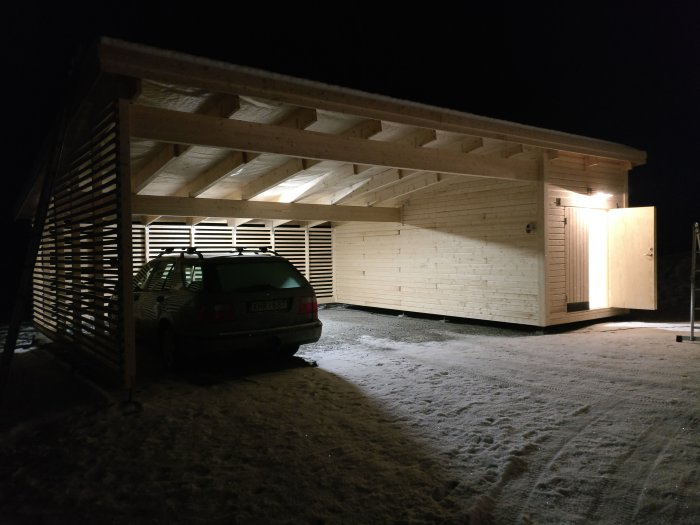 Bil parkerad under nybyggd carport med takbelysning på kvällstid.