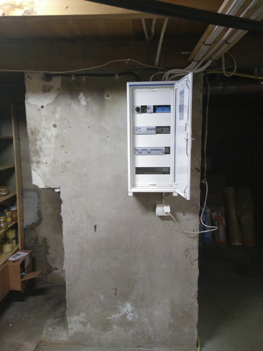 Ett nyinstallerat elskåp på en oputsad vägg i ett källarrum med synliga kablar uppe till höger.