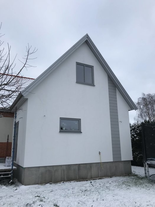 Nästan färdigt hus med vit fasad och snö på marken, redo för trädgårdsarbete.