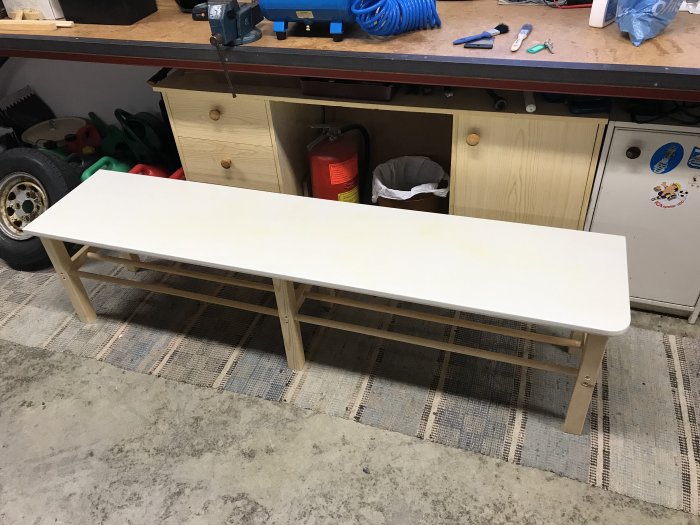 Platsbyggd vit sittbänk med gulflagning i lacken, placerad i ett stökigt garage.