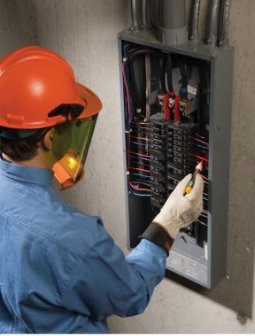 Elektriker i arbetskläder och hjälm installerar el i ett elektriskt servicepanel i USA.