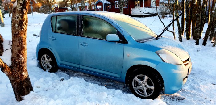 Blå personbil parkerad i snö med frostiga fönster och soluppgång i bakgrunden.