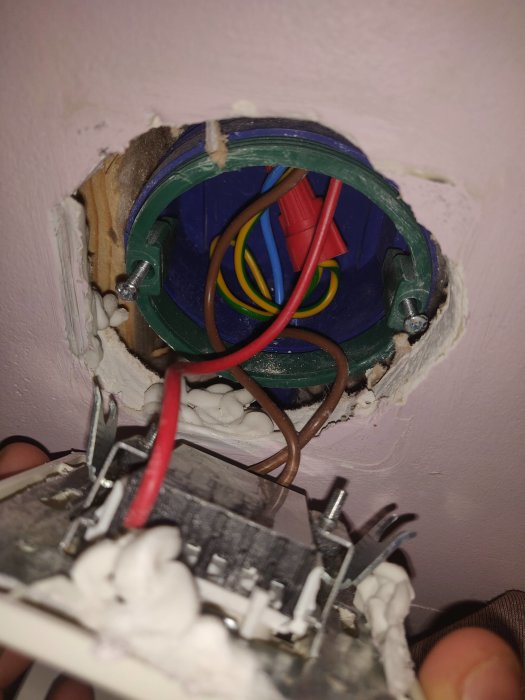 Öppen eldosa i vägg med synliga elkablar och otillräcklig isolering, visar dåligt installationsarbete.