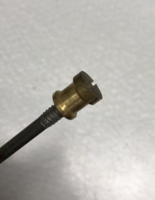 Förstaänden av en skruv med mässingsknopp och räfflad stång på en vit bakgrund.