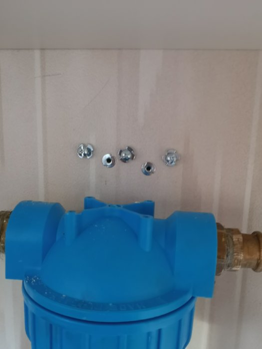 Blå vattenfilterkoppling installerad på ett rör med fyra fästelement ovanför.