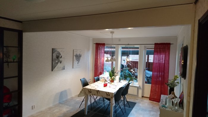 Matsal med dukat bord, taklampa, konst på väggarna, och röda gardiner framför glasdörrar som leder ut.
