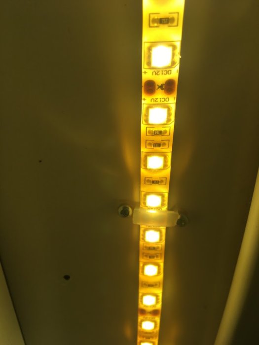 Gulaktig LED-strip monterad på en yta, med ojämn belysning och färgskiftning längs stripen.