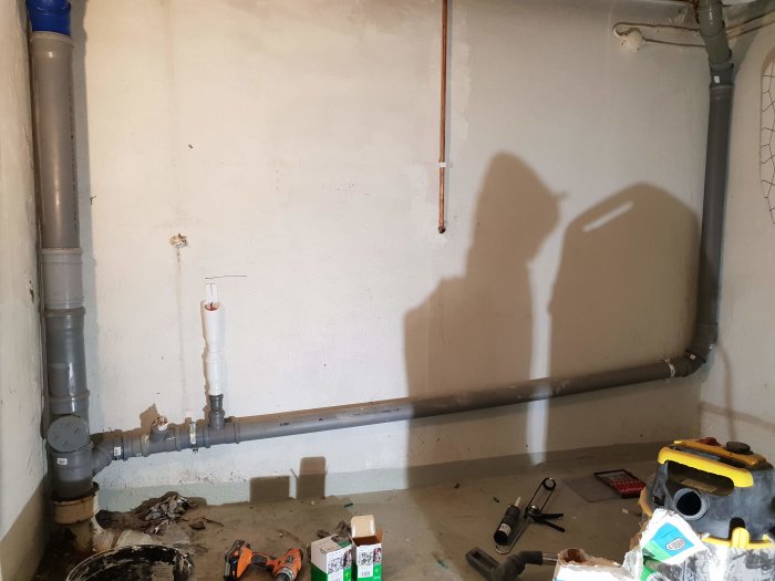 Renoverat avloppssystem med nya rör i ett betongrum, verktyg och material på golvet.