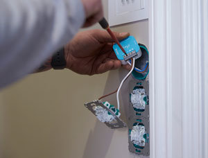Person kopplar in en blå elektronisk enhet i vägg med flera osammanfogade uttag.