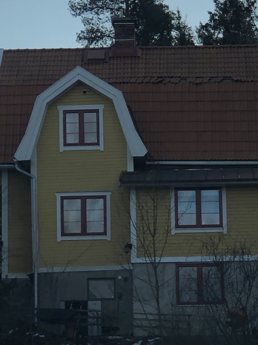 Takpannor som lossnat längs takbrytet på ett gult hus med tegeltak efter storm.