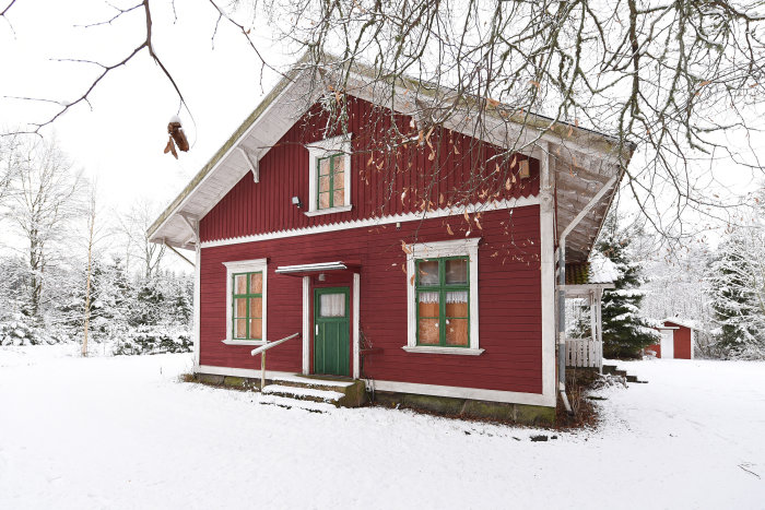 Gammalt rött stationshus med vita knutar och gröna fönsterluckor under ett snötäckt landskap.