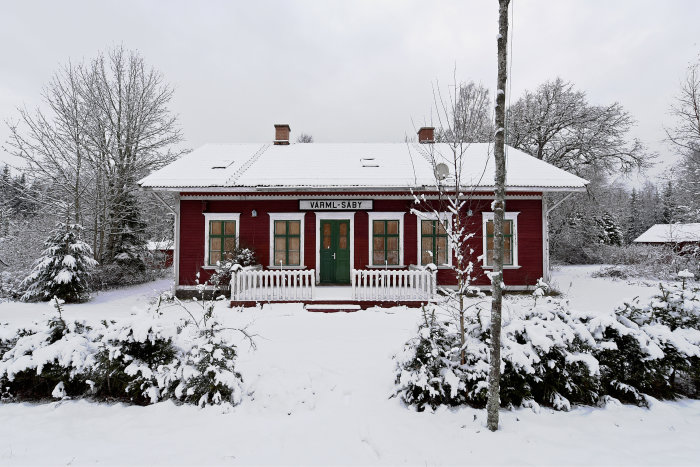 Gamla Värmlands-Säby stationshus i rött med vit snö, omvandlat till bostad, i vinterlandskap.