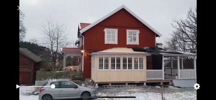 Rött hus med delvis blåst bort underlagsduk på taket efter stormen Alfrida, med synlig snö och en bil framför huset.