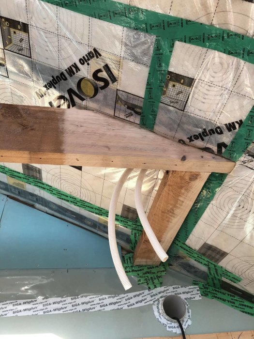 Tak under konstruktion med plastfolie, isoleringstejp och en slipad takstol i förgrunden.