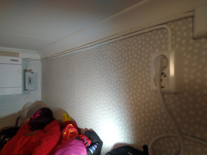 Elcentral och nyinstallerat uttag med elmätare ovanför en hatthylla med kläder och väskor.